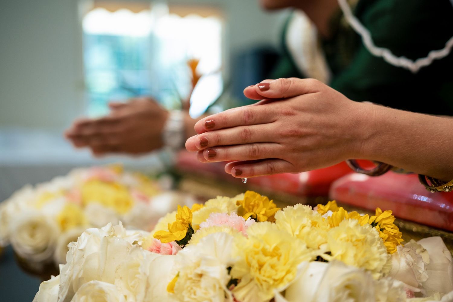 Close-up of hands in prayer position over white and yellow flower arrangements at Thai wedding ceremony.