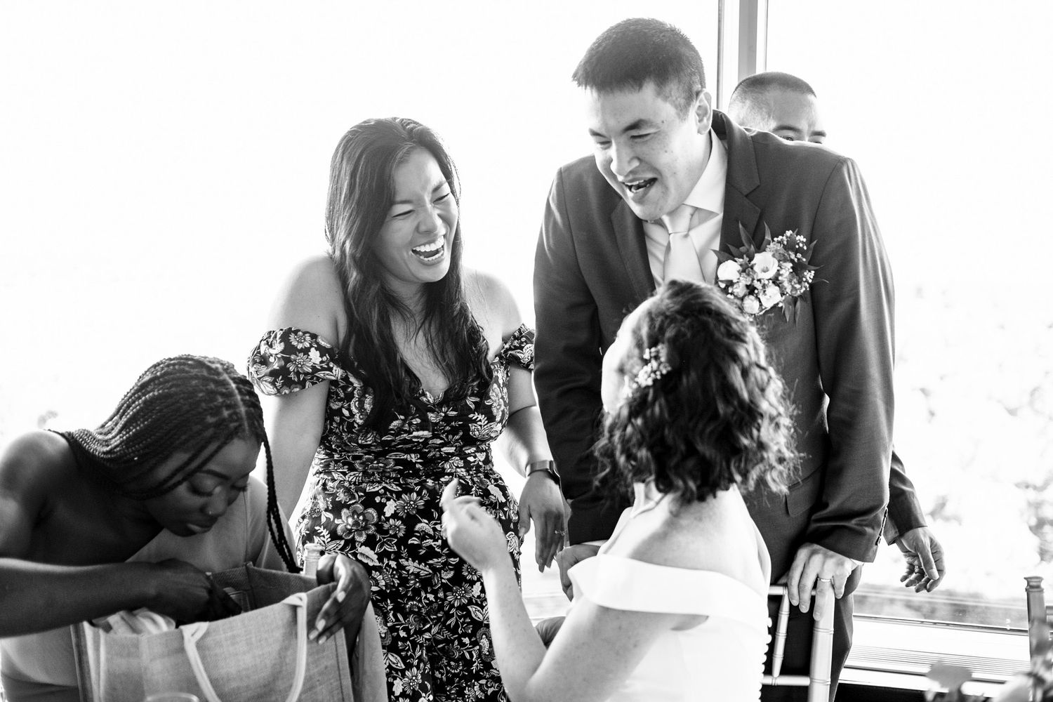 Groom laughing with guests in floral dress at wedding reception celebration.