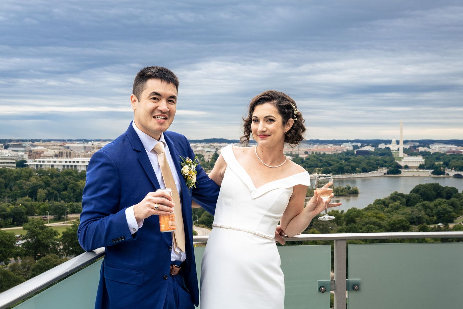 Bride and groom toast with champagne on a rooftop overlooking the Washington DC skyline on their wedding day.