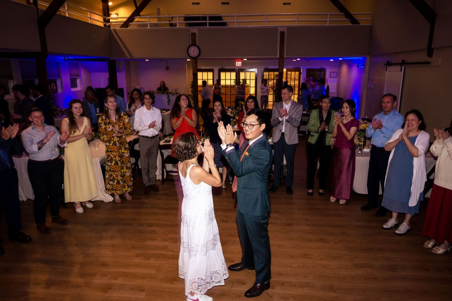 Bride and groom share first dance while wedding guests clap in a circle around them.