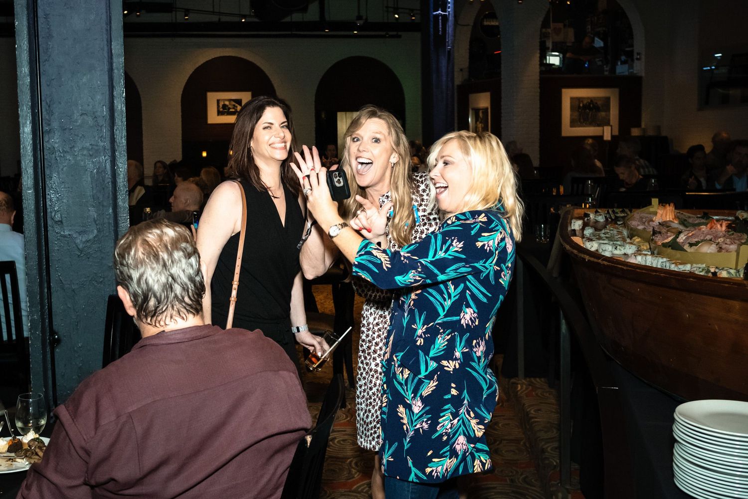 Three women laughing and celebrating together at a restaurant event party.
