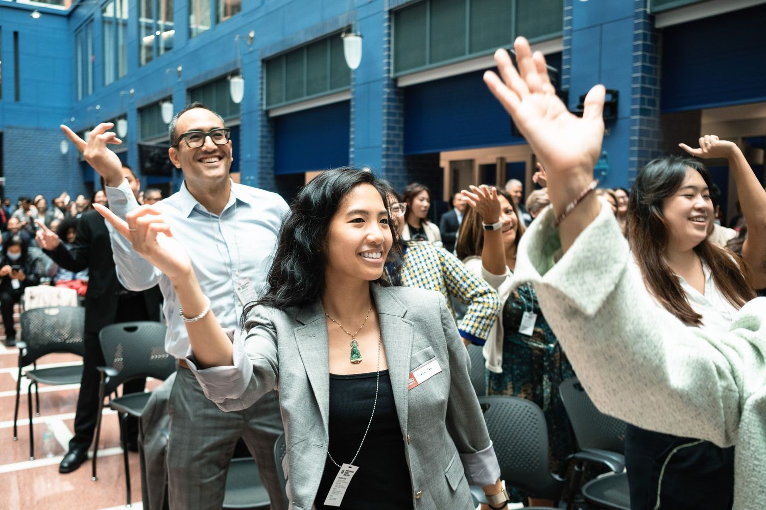 Diverse group of excited people raising hands and smiling at an indoor event or conference gathering.