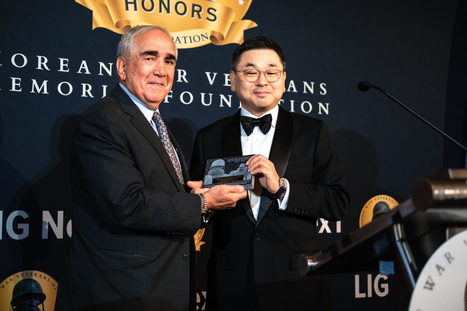 Two men in formal suits pose together at the Korean War Veterans Memorial Foundation Honors gala with an award.