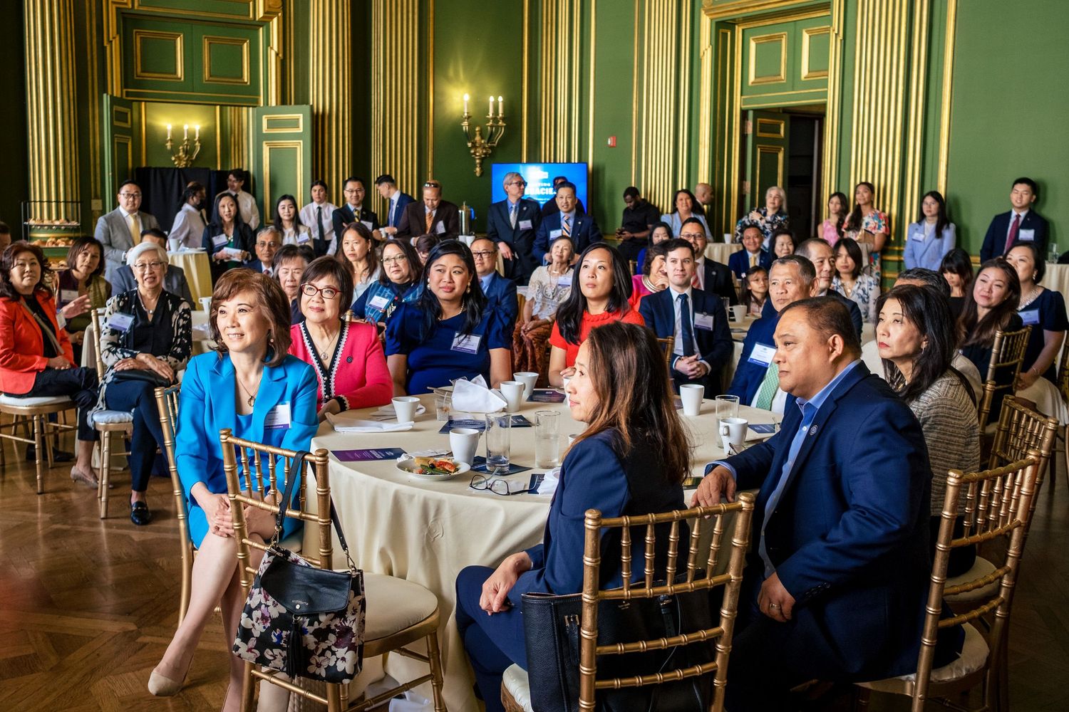 Diverse group of professionals attending a formal conference or gala event in an elegant green-walled ballroom.