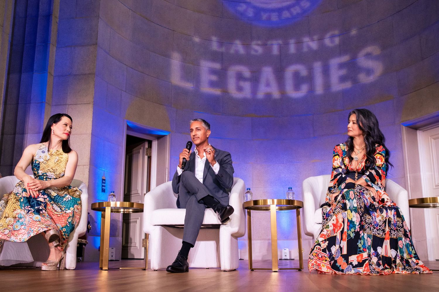 Three panelists discuss on stage at Lasting Legacies event, seated in white chairs under blue lighting.