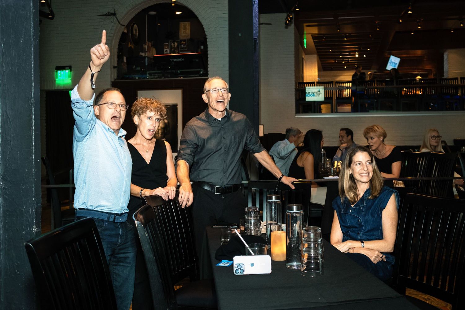 Group of friends laughing and celebrating at a restaurant bar during a lively social event.