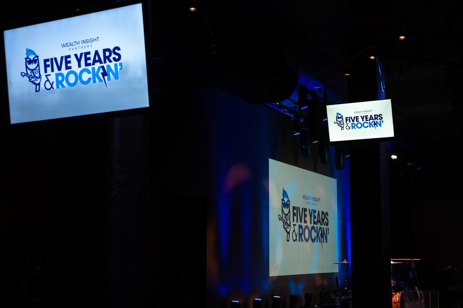 Event stage displaying 'Five Years & Rockin' anniversary celebration signage with blue lighting at a corporate conference.