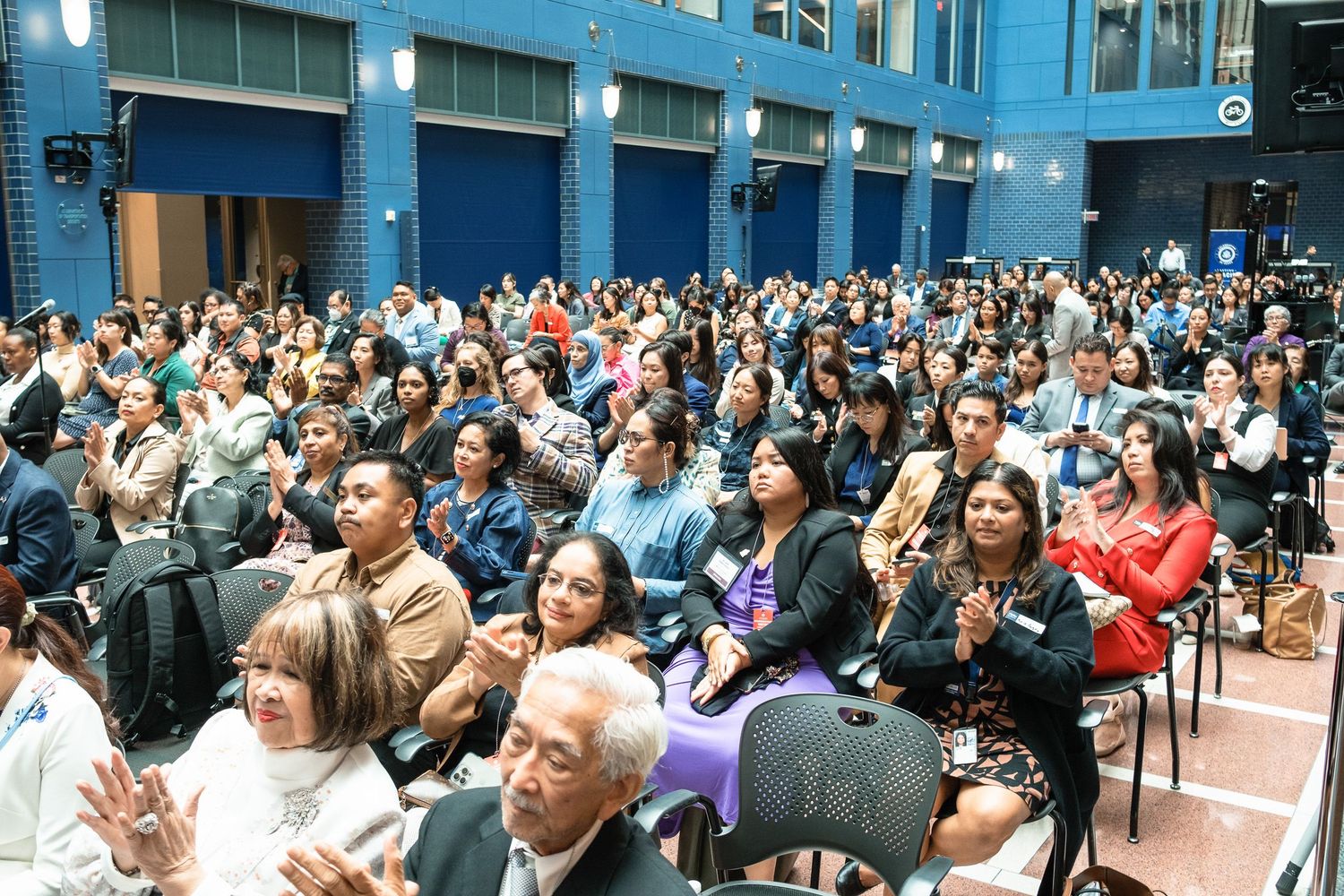 Large crowd of diverse attendees applauding at an indoor event held in a modern blue-accented venue.