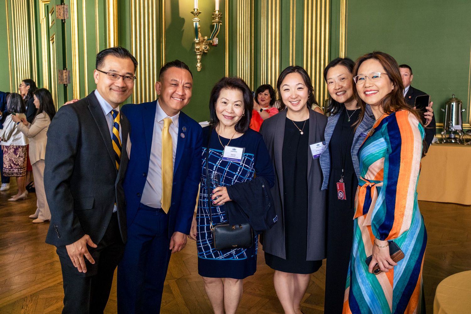 Group of six professionals posing together at a formal event in an elegant green-walled venue.