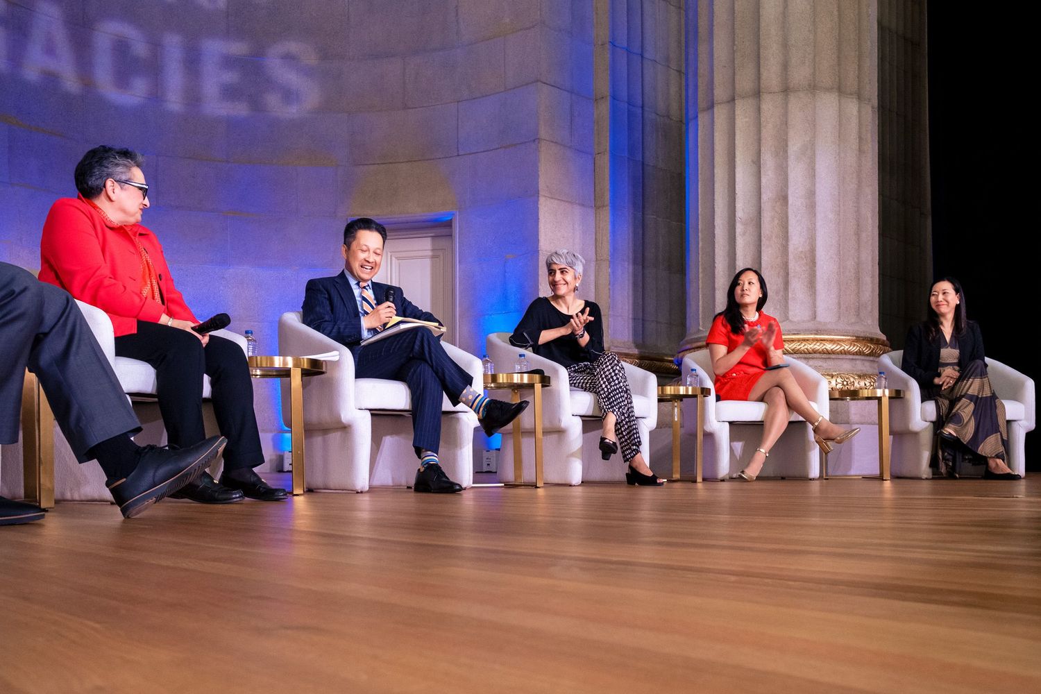 Panel of six speakers seated on stage at a formal conference discussing democracy topics.