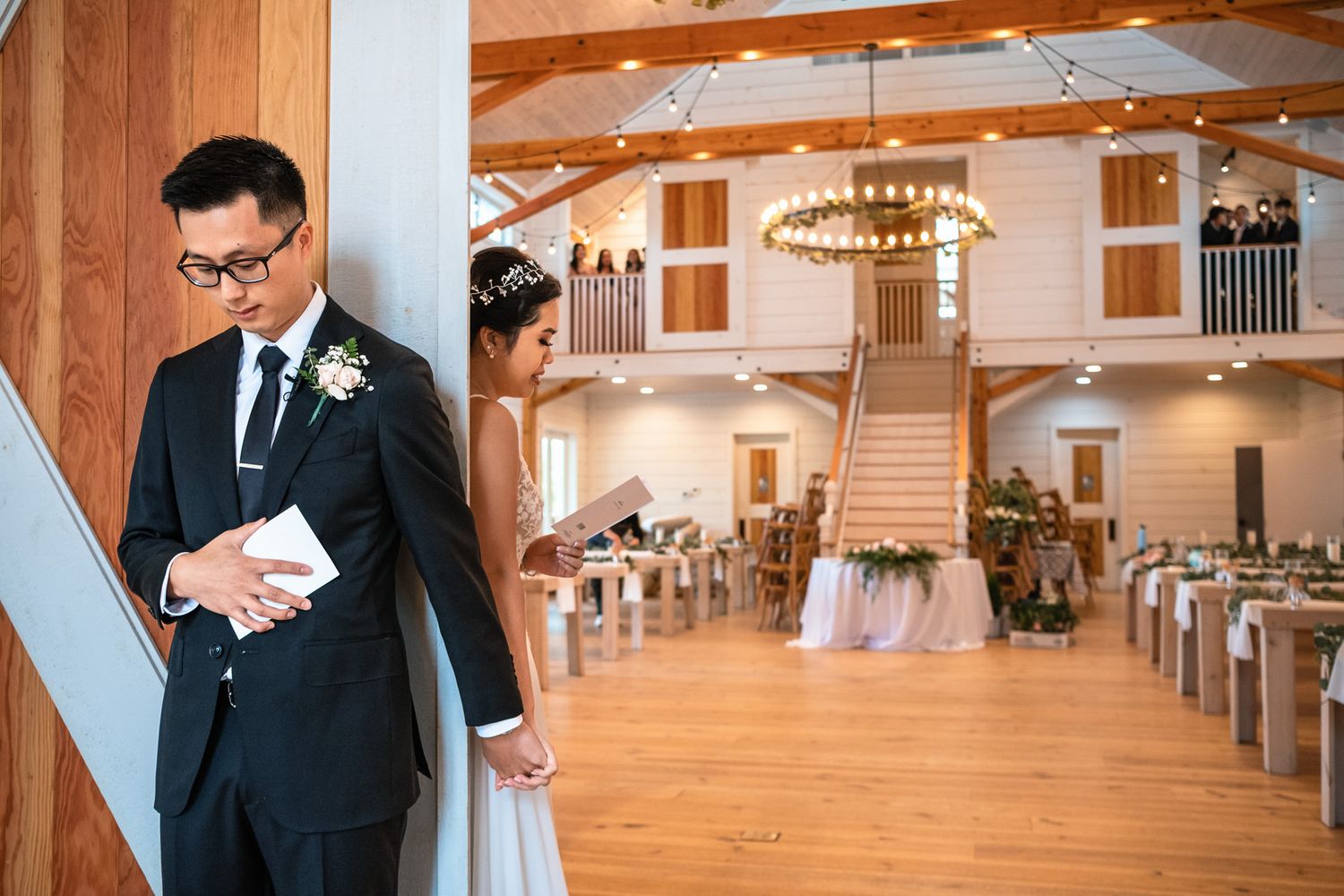 Groom reads vows while bride waits around corner in a beautifully decorated rustic barn wedding venue.