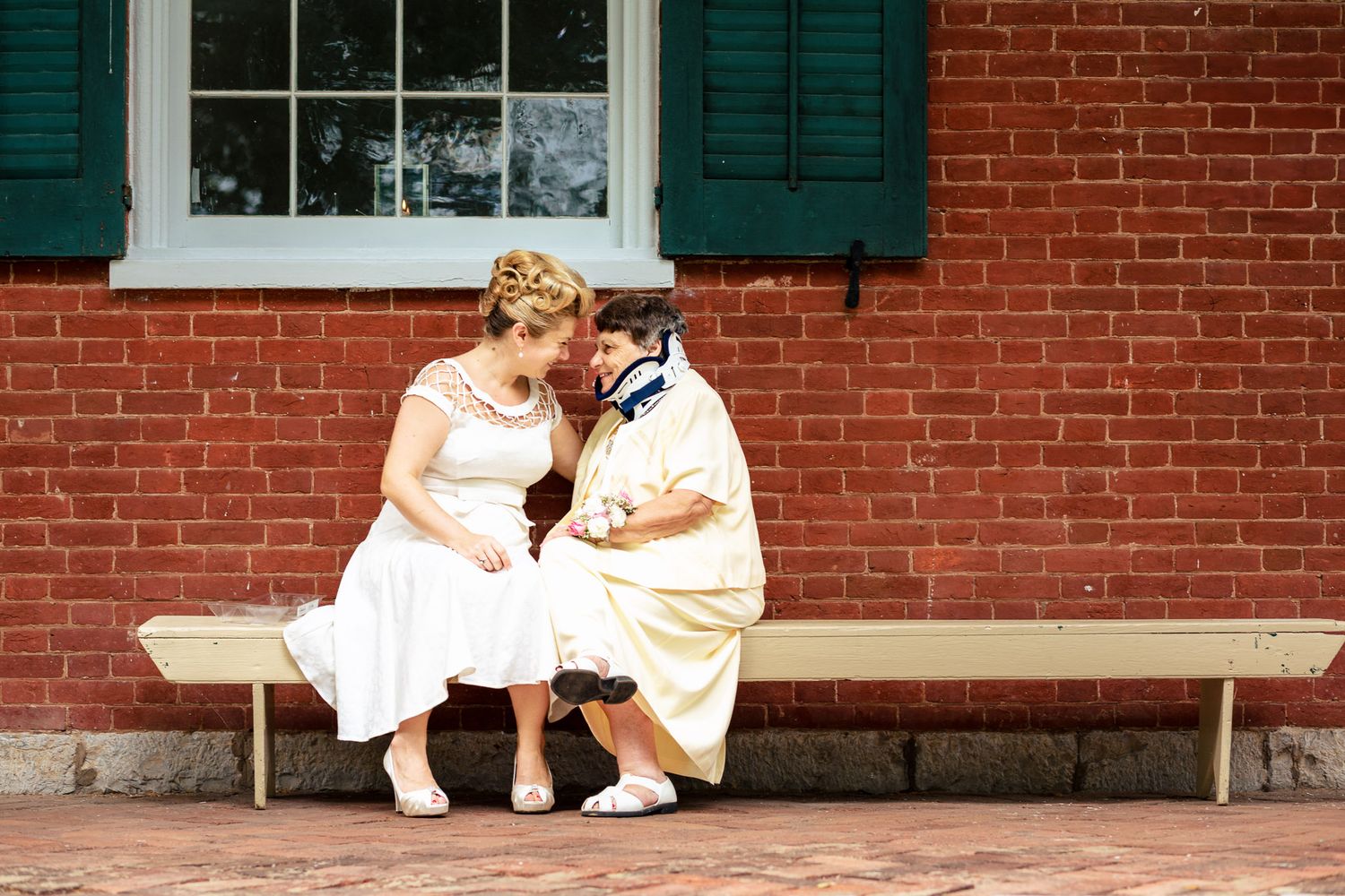 Bride and groom share an intimate moment sitting on a bench against a brick wall.