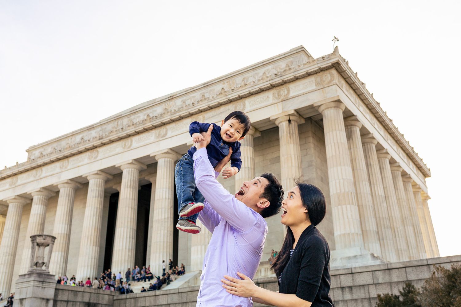 Asian family lifting toddler in front of the Lincoln Memorial in Washington DC.