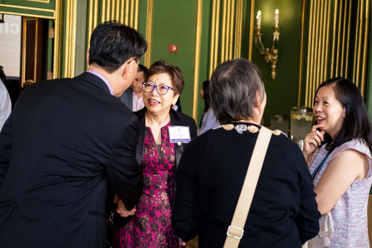 Group of elegantly dressed professionals networking and conversing at a formal indoor reception event.