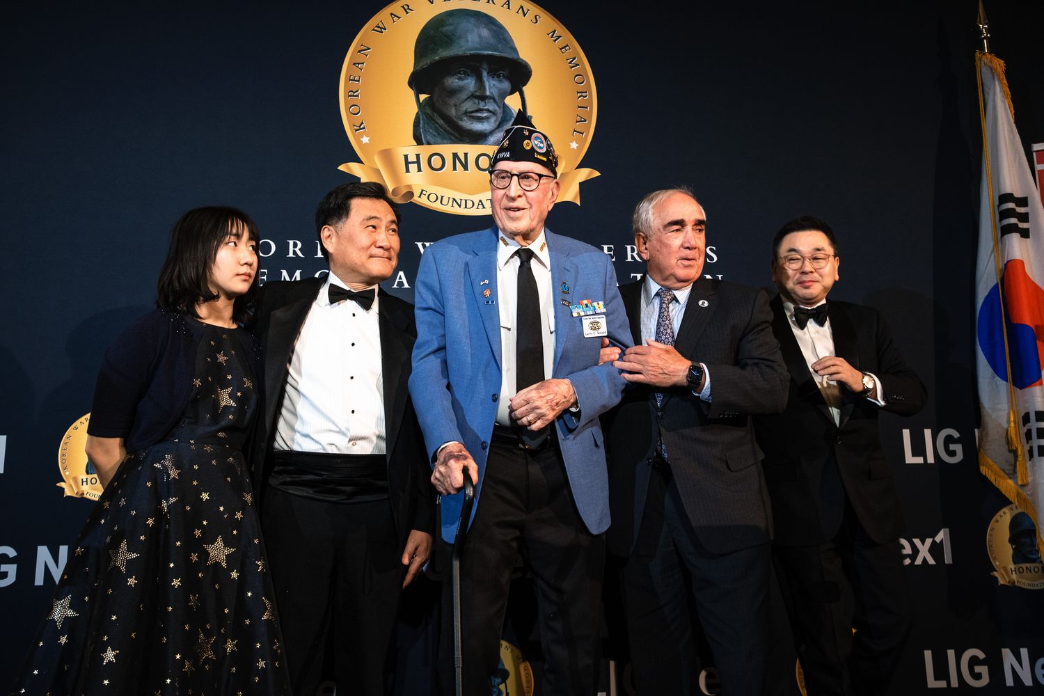 Five people pose together at Korean War veterans honor ceremony in front of commemorative backdrop.