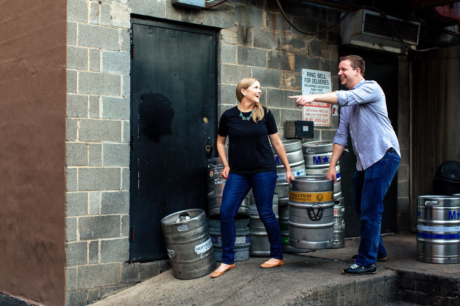 Man and woman talking near beer kegs outside a bar entrance on a city street.