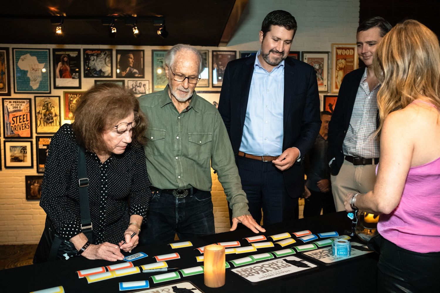 People gathered around a table with colorful cards at an art gallery event with framed posters on the wall.