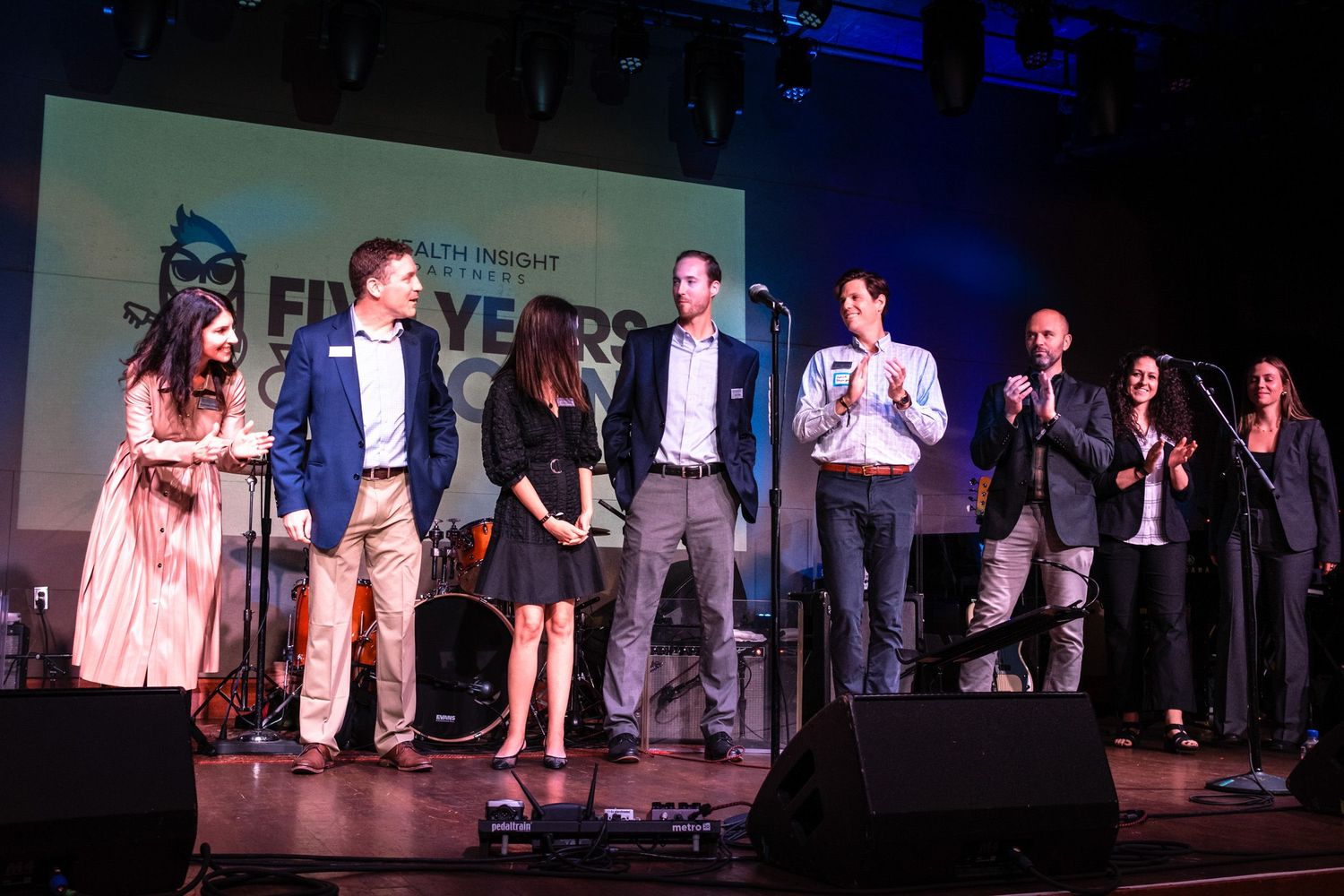 Group of professionals on stage at a corporate awards ceremony with colorful backdrop lighting.