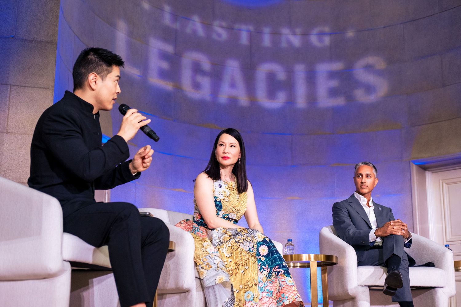 Three panelists discuss at Lasting Legacies event on stage with blue backdrop.