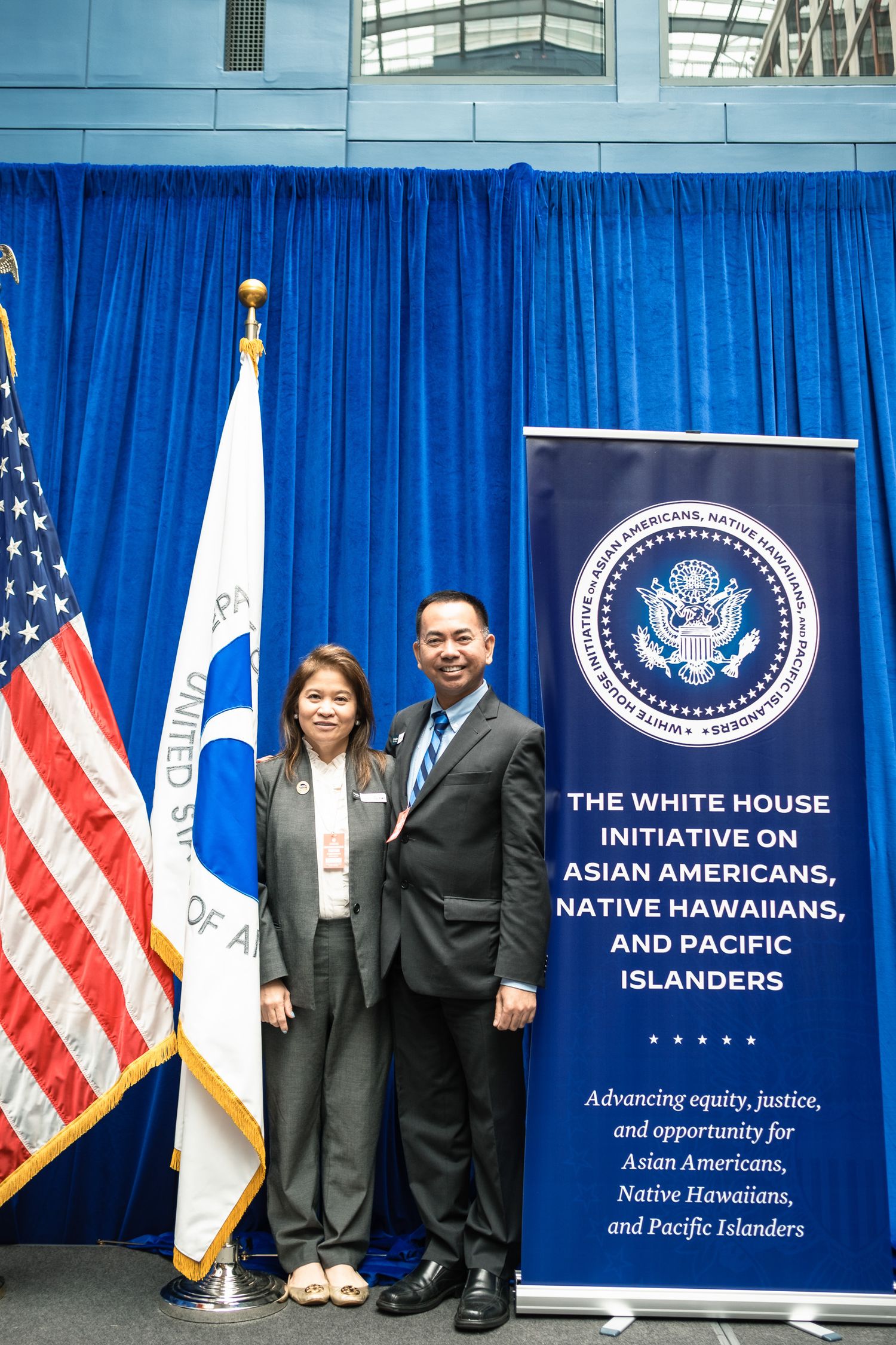 Two people pose beside a White House Initiative on Asian Americans, Native Hawaiians, and Pacific Islanders banner.