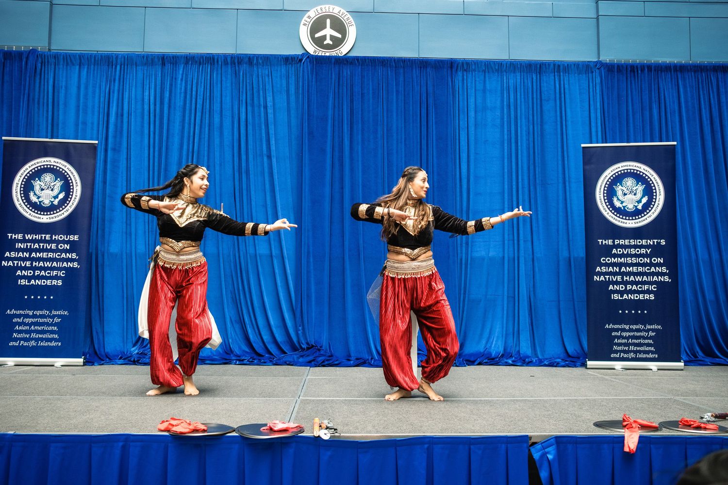 Two Indian classical dancers in red and gold costumes perform on stage at a White House cultural event.