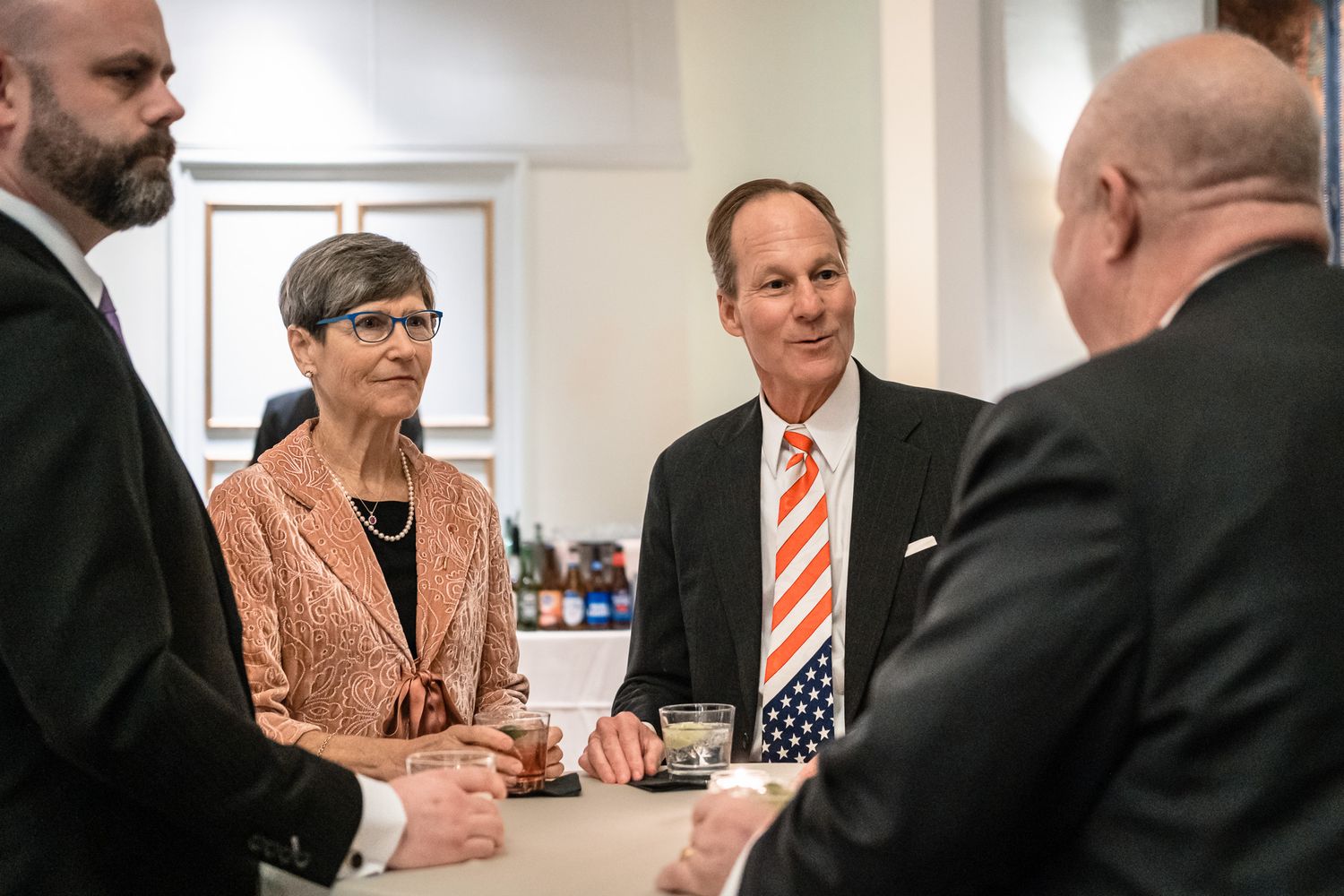 Four professionals in formal attire networking around a high-top table at an elegant reception event.