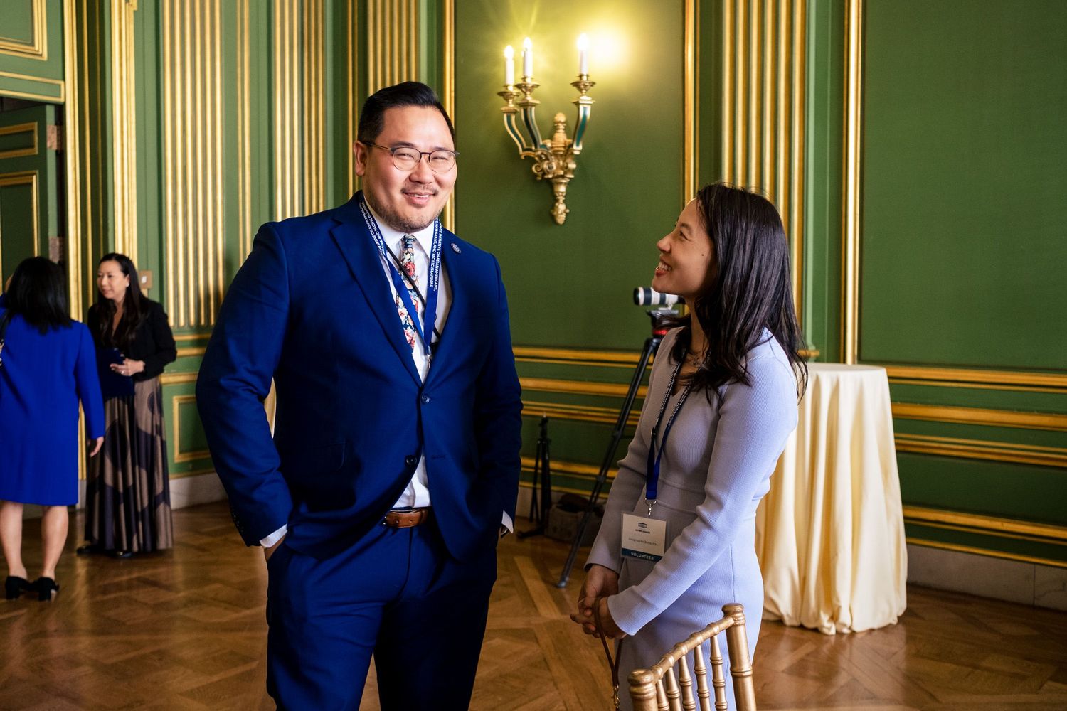 Two professionals networking in an elegant green and gold ballroom at a formal conference event.