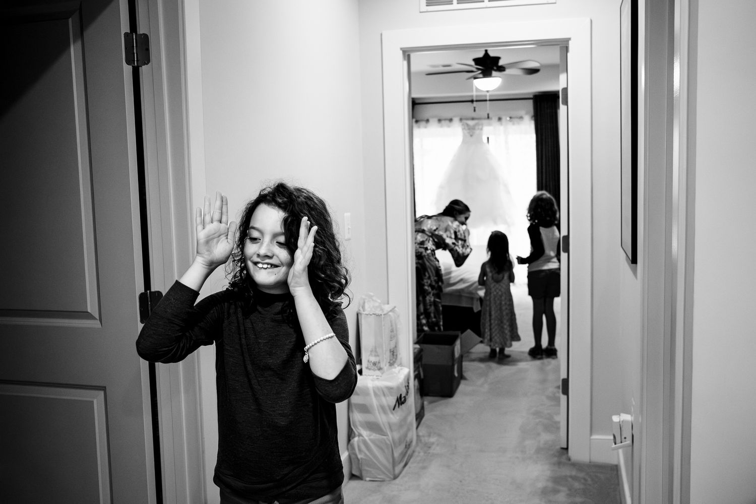 Young girl smiling in hallway while bride prepares in background in black and white.