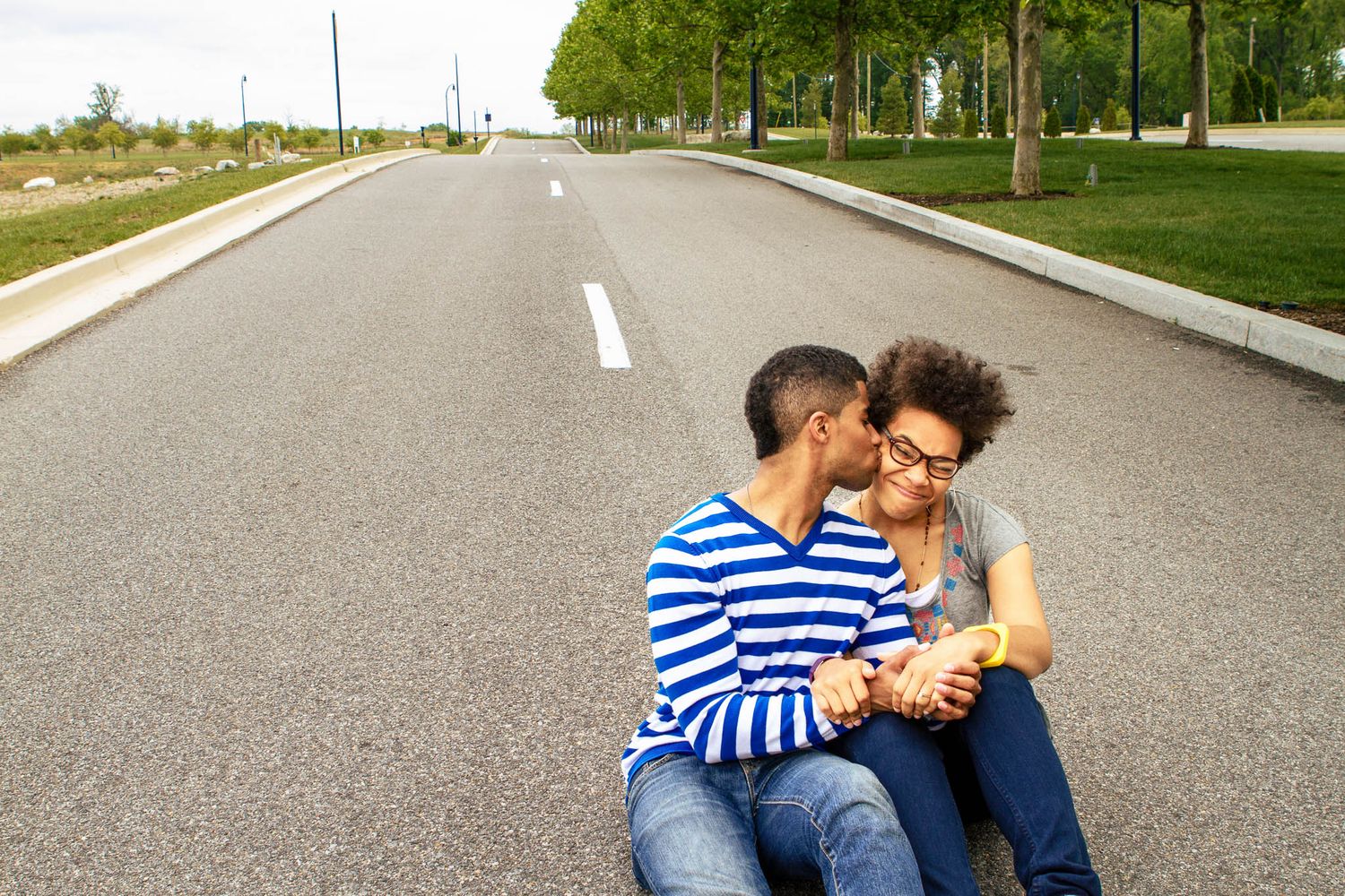 Young couple sitting together on an empty road sharing a tender kiss in a park setting.