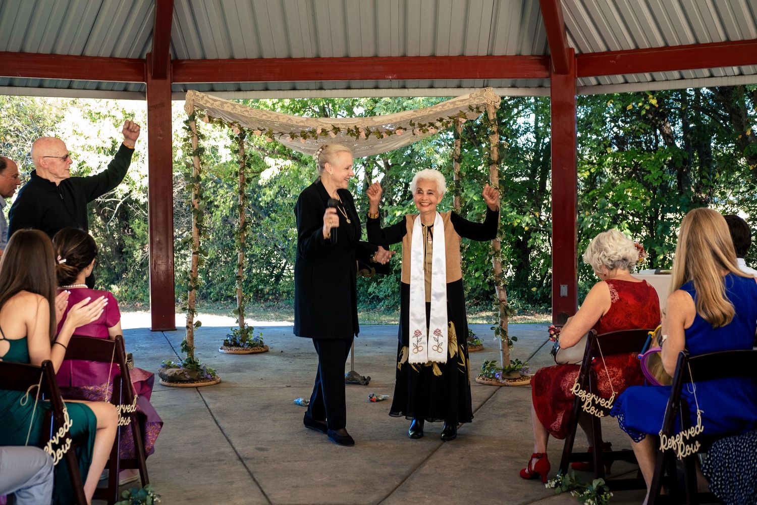 Wedding officiant raises glass in toast during intimate outdoor gazebo ceremony with guests.