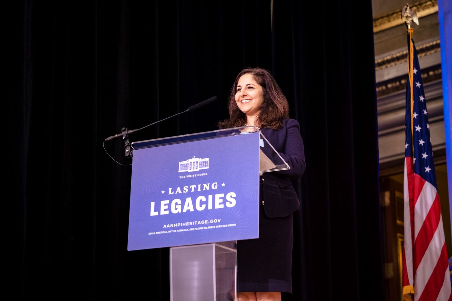 Woman speaking at podium during Lasting Legacies event with American flag backdrop.