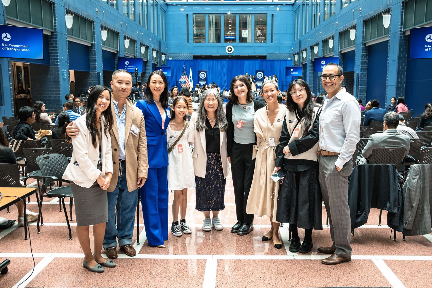 Group of people posing together at a graduation white coat ceremony in a blue decorated university hall.