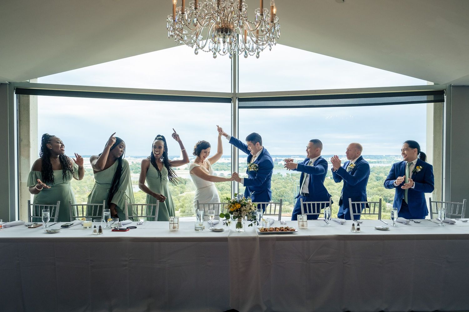 Wedding party celebrates at the head table with a panoramic view through large windows at the reception.