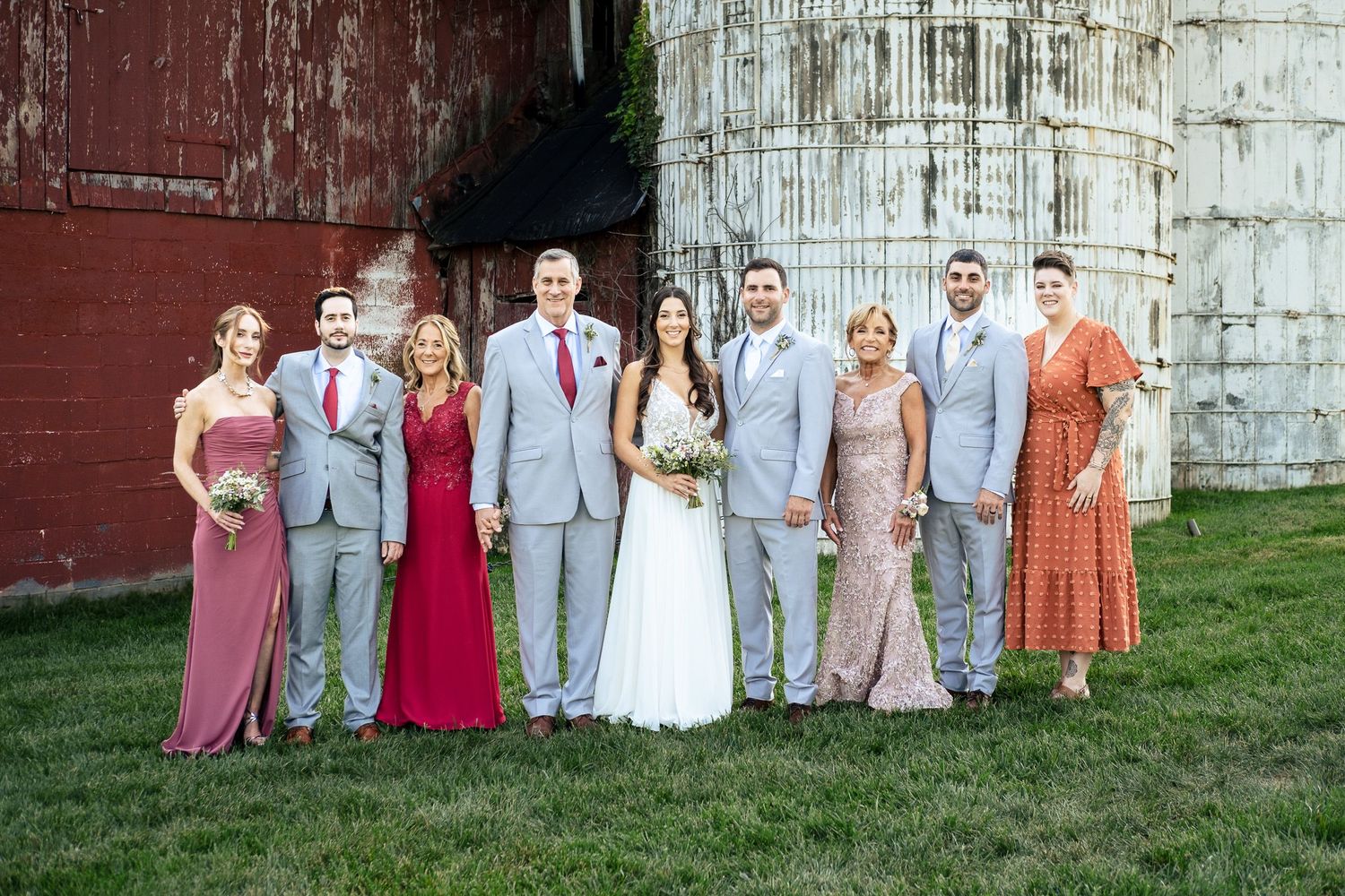 Wedding party and family pose together in front of a rustic red barn and stone silo.