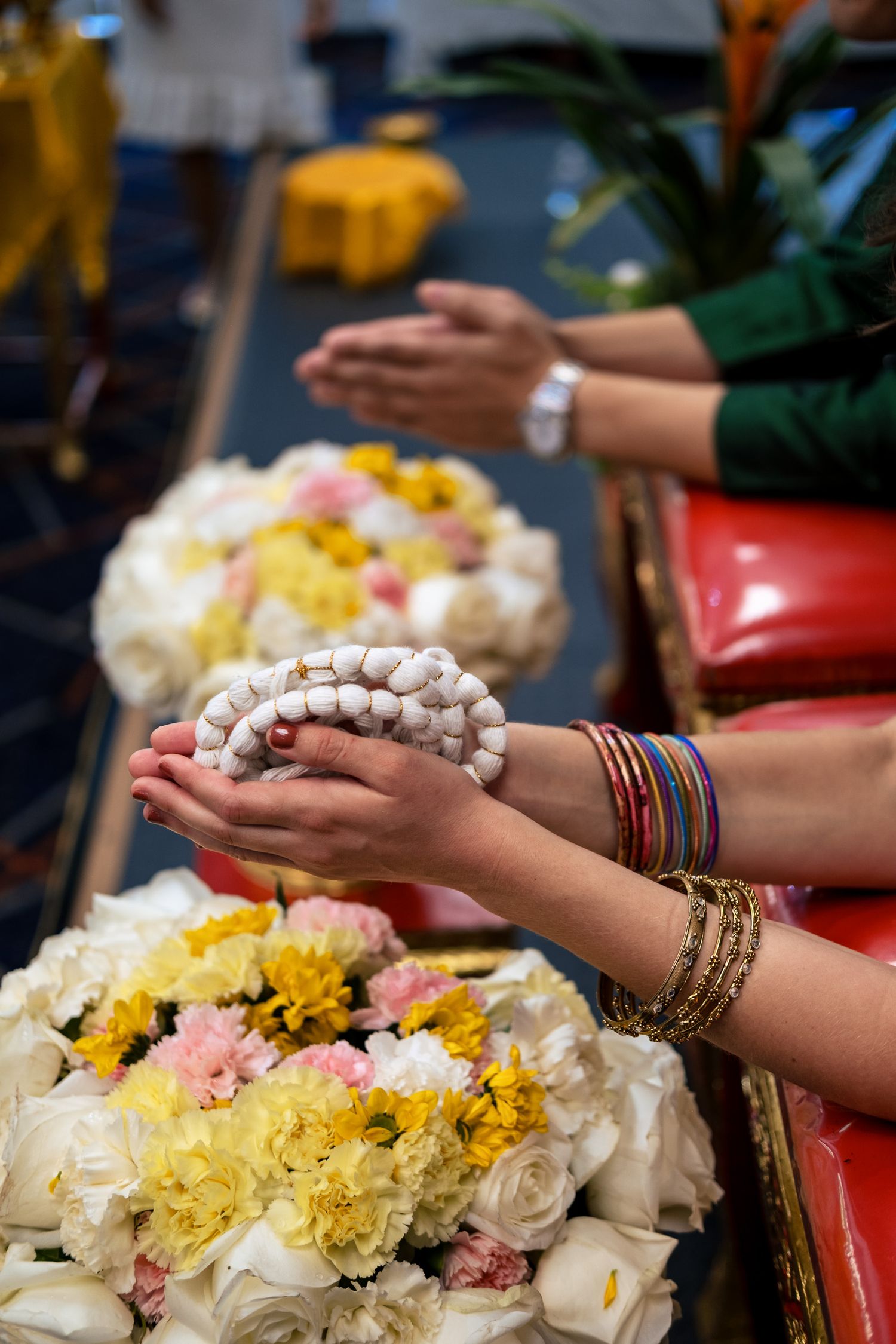 Hands holding white jasmine garland over colorful flowers at traditional Thai wedding ceremony.