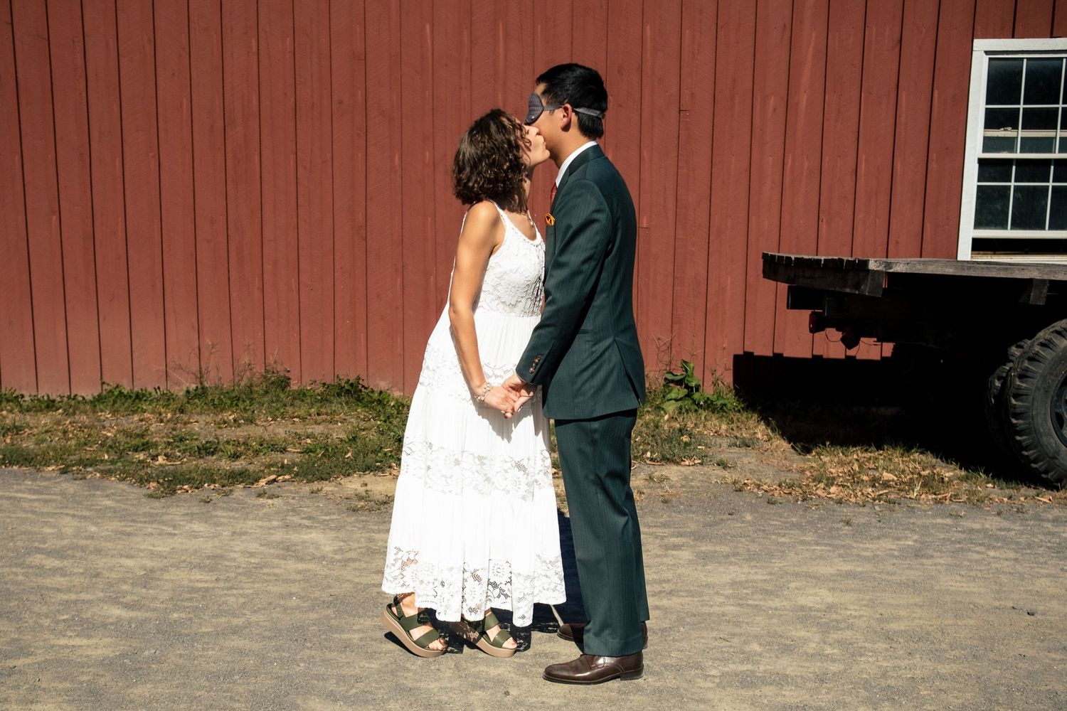 A couple shares a romantic kiss in front of a red barn on their wedding day.
