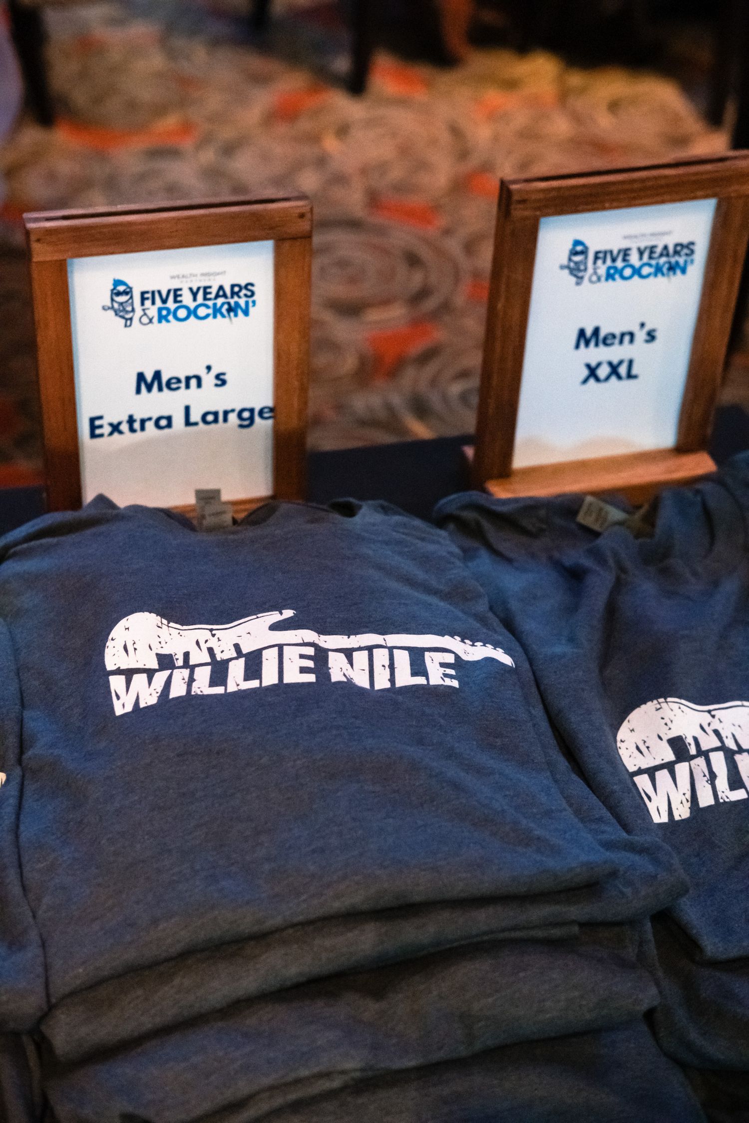 Willie Nile band merchandise t-shirts in Men's XL and XXL sizes displayed at a Five Years & Rockin' event.