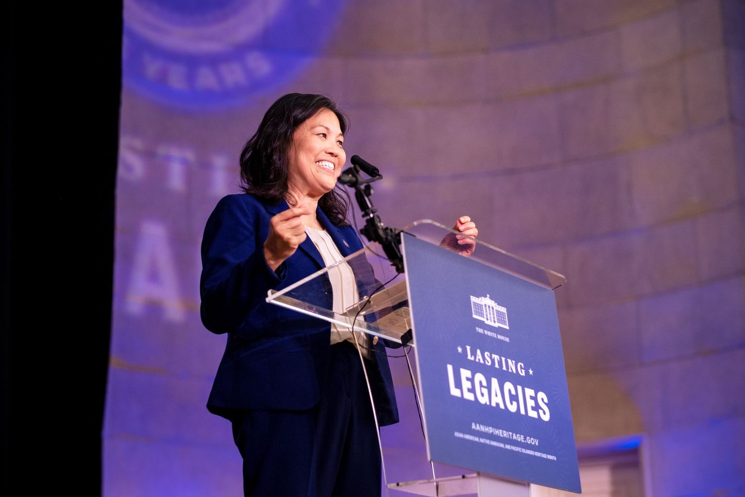 Woman in blue suit speaks at podium with Lasting Legacies sign at formal awards event.