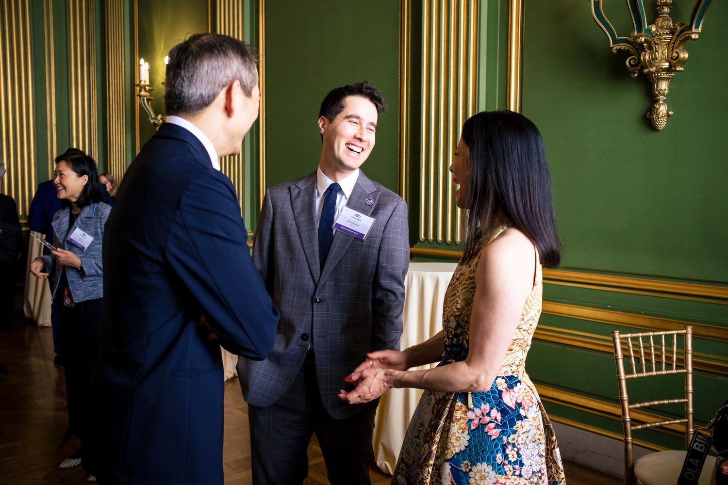 Three professionals networking and laughing at a formal event in an elegant green-walled venue.
