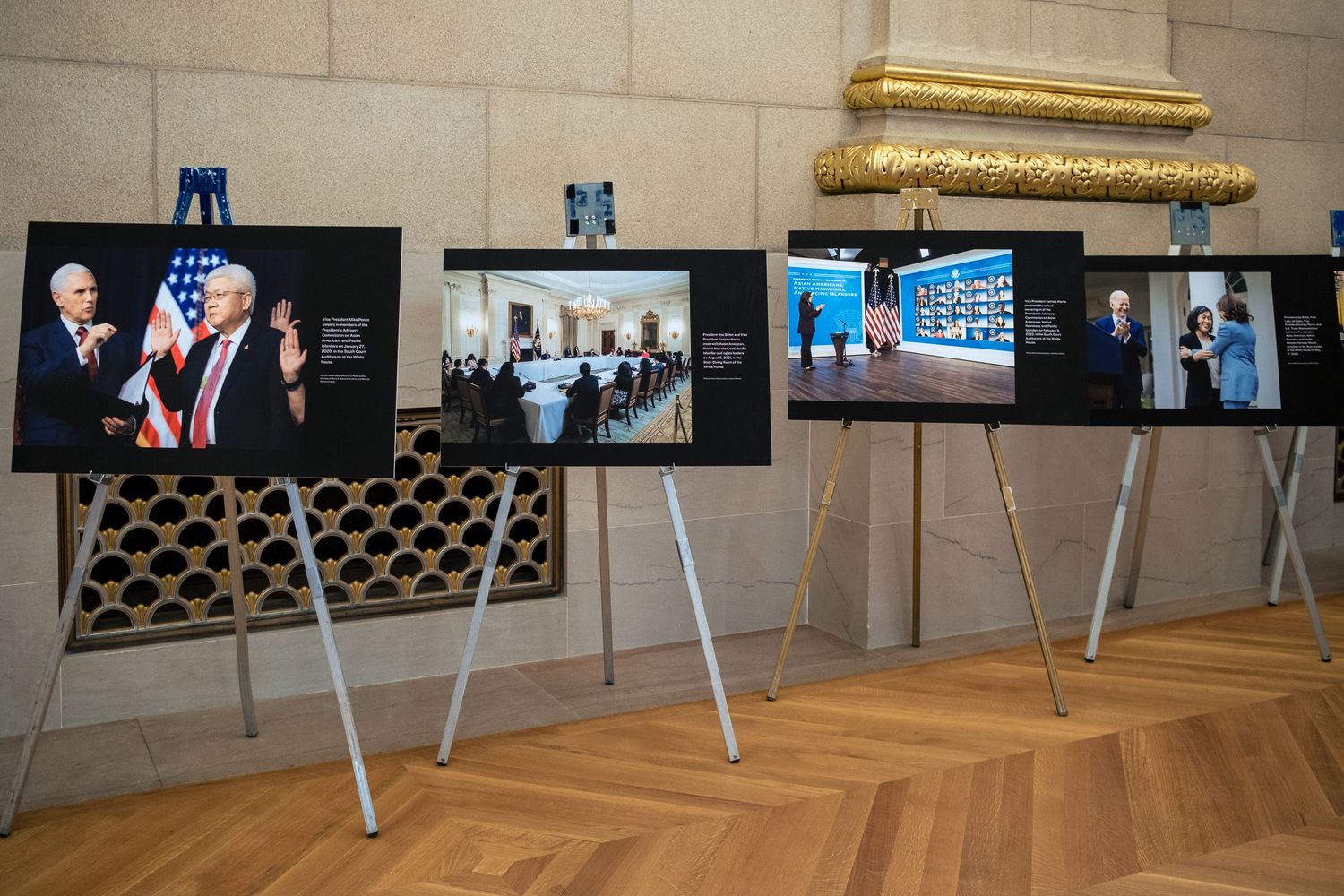 Photo exhibition displaying large prints of political events on easels in an elegant hall with wooden floors.