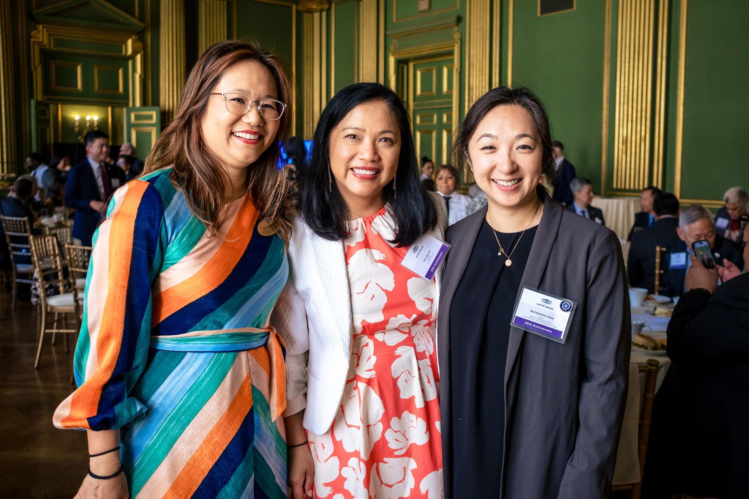 Three smiling women pose together at an elegant green-walled banquet hall event.