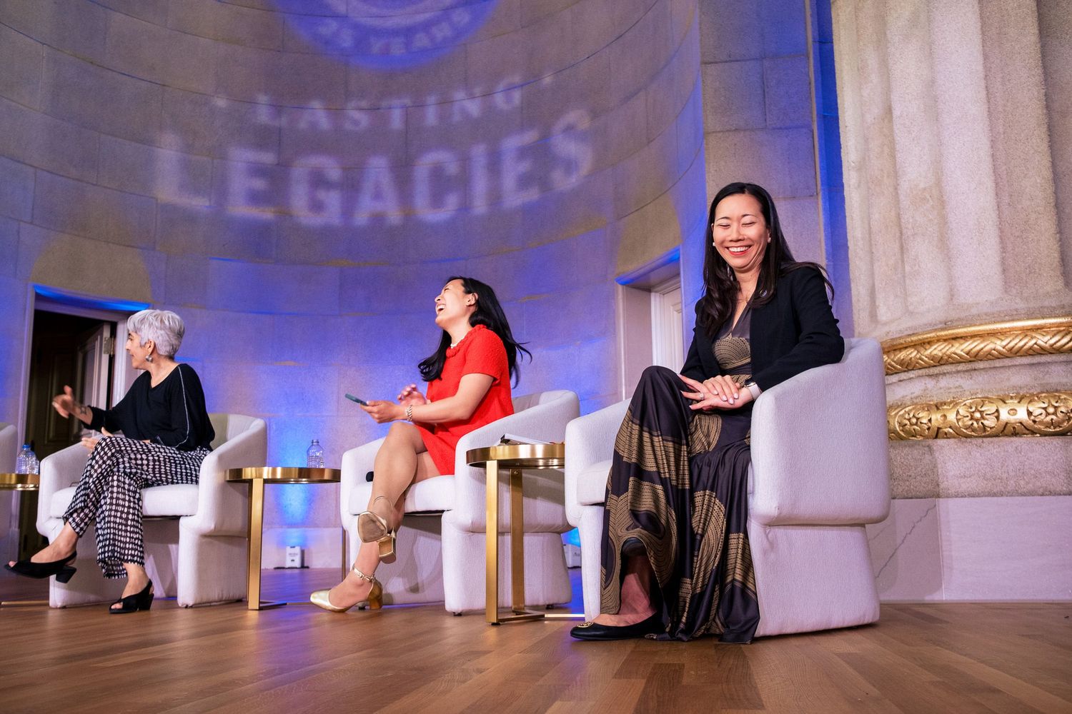 Three women engage in a panel discussion at a Lasting Legacies event, seated in white chairs on an elegant stage.