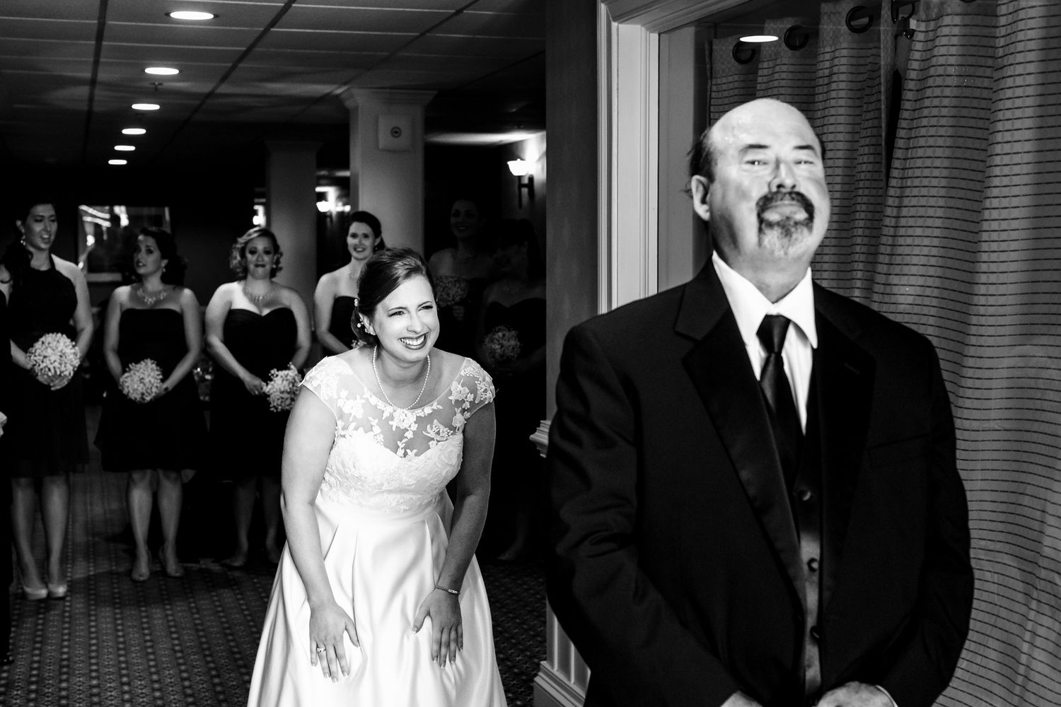 Black and white photo of smiling bride walking with suited man at wedding.