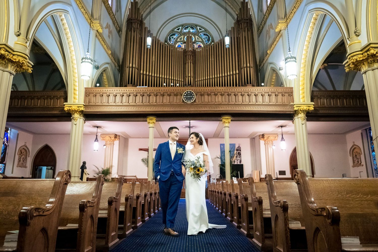 Bride and groom stand together in a stunning church aisle with a grand pipe organ backdrop.