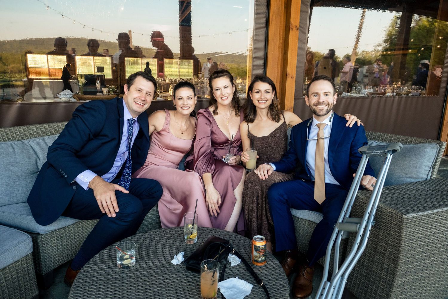 Five elegantly dressed wedding guests smile and pose together on an outdoor patio lounge area.