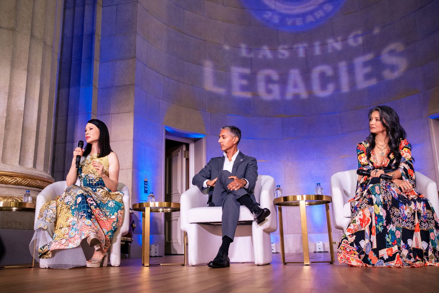 Three panelists seated on stage at a Lasting Legacies event under blue lighting.