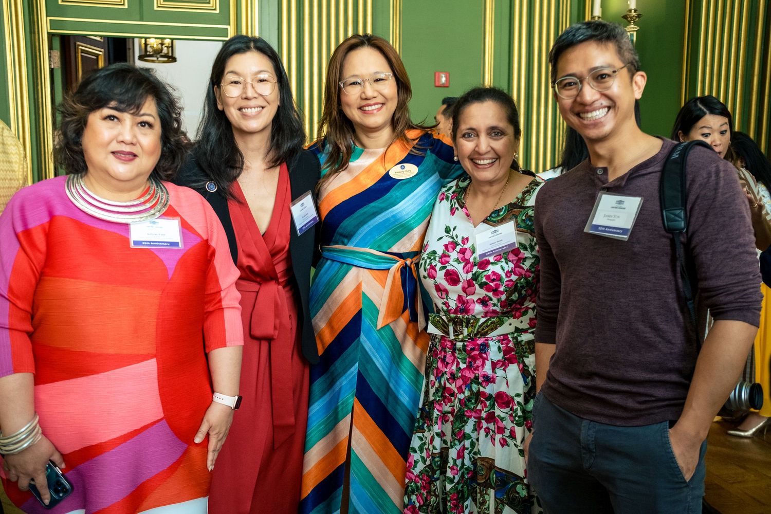 Five people smiling and posing together at a formal event in an elegant green-walled venue.