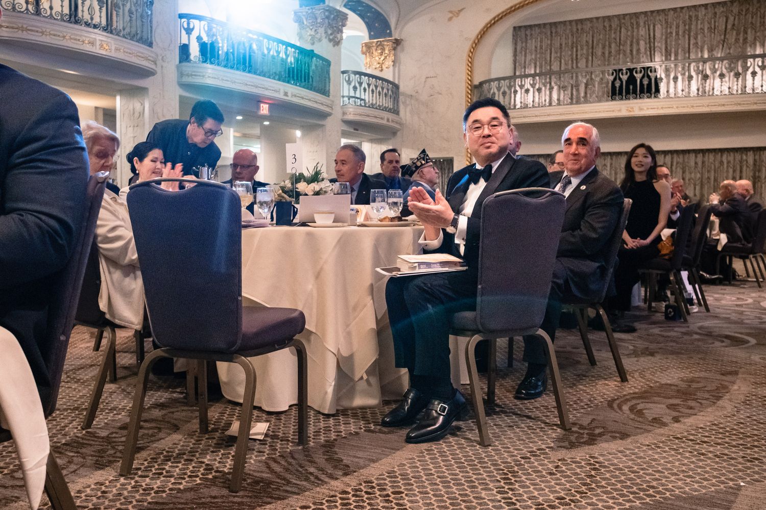 Guests in formal attire seated at elegantly set tables during a grand ballroom gala dinner event.