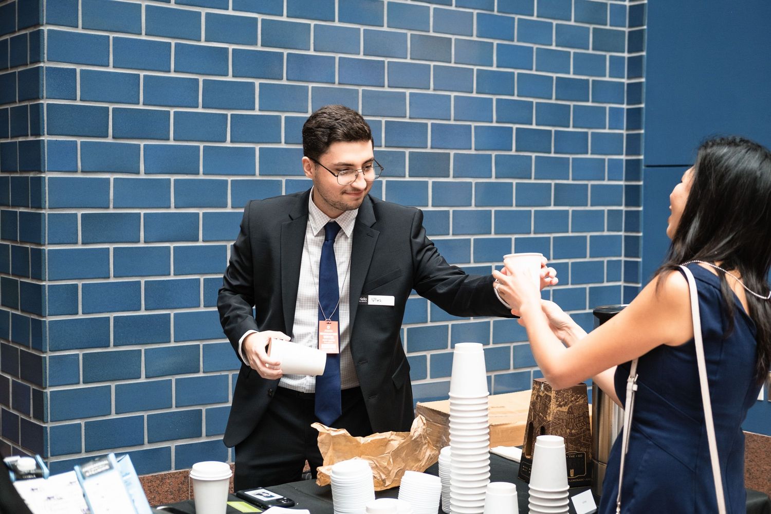 Professional man in suit serving coffee at a networking event near a blue tiled wall.