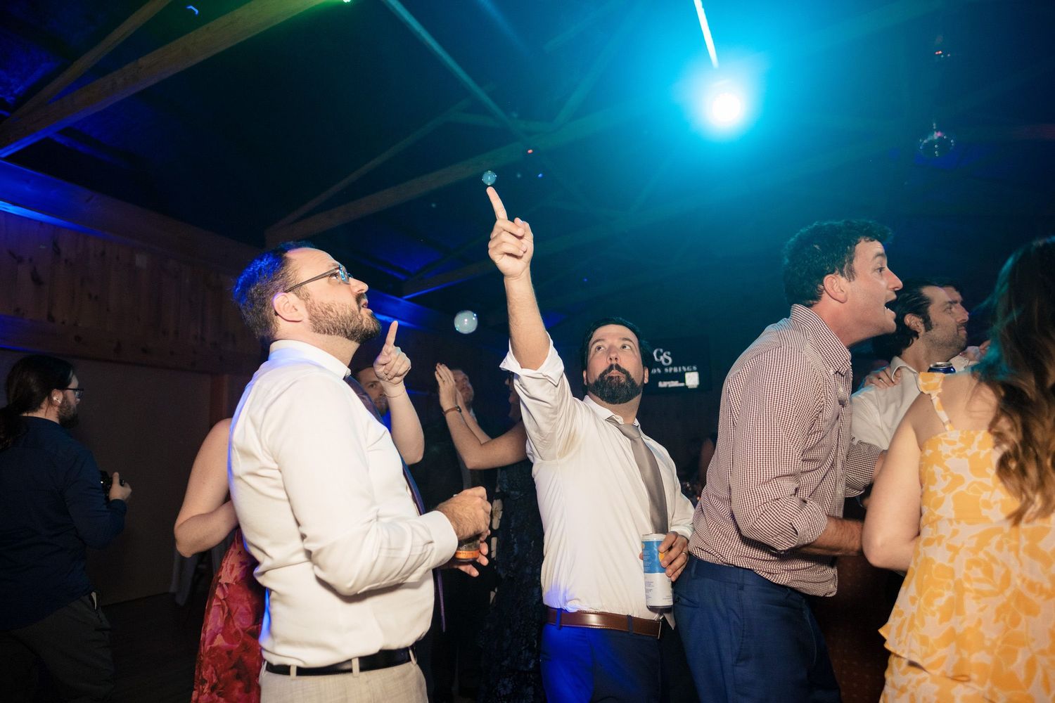 Excited wedding guests dancing and celebrating under blue lights at an indoor reception party.